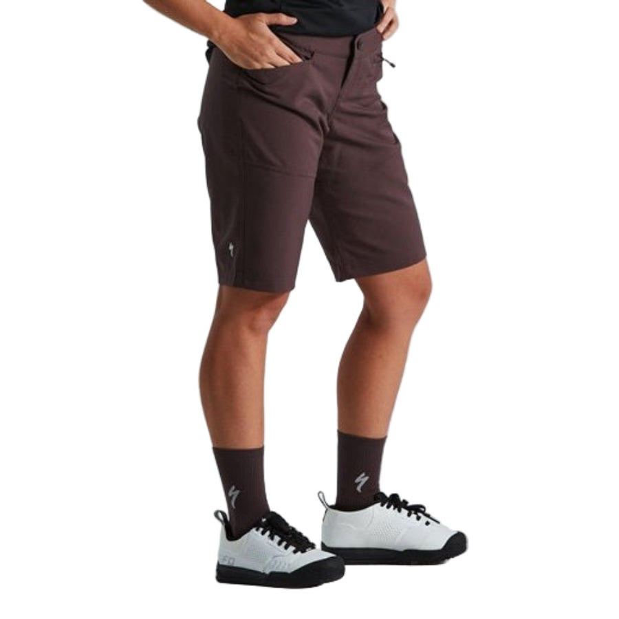 Person wearing brown shorts, black socks, and white sneakers on a light gray background