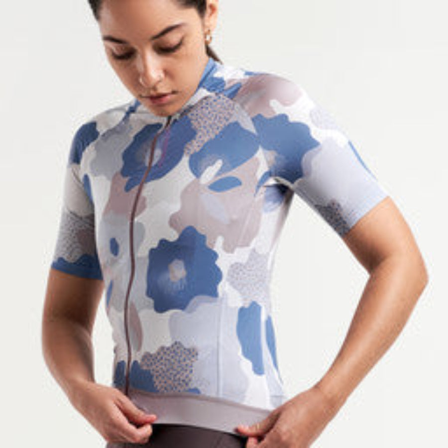 Woman wearing a patterned PEPPERMINT cycling jersey on a plain background