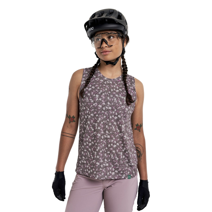 Person wearing a Peppermint Cycling floral sleeveless shirt, helmet, and gloves on a white background.