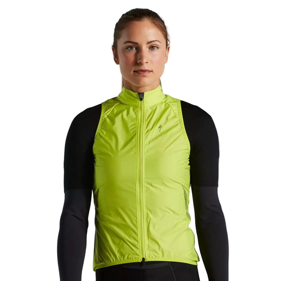 A woman wearing a bright yellow specialized hyperviz vest over a black long-sleeve shirt on a light gray background