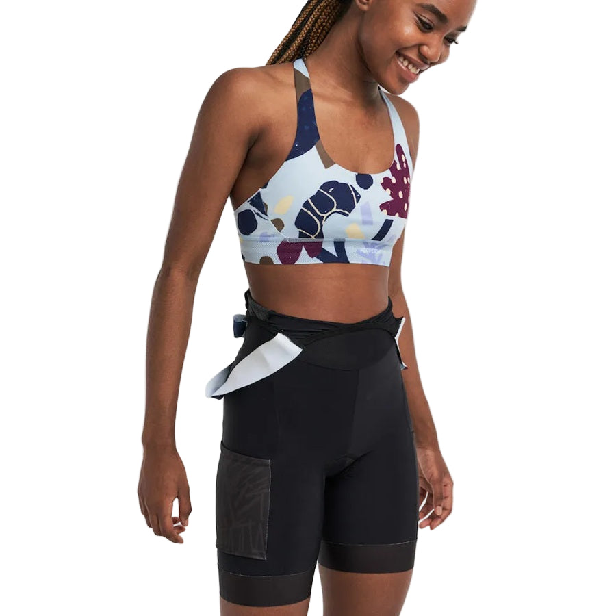 Woman wearing a colorful sports bra and black shorts on a white background